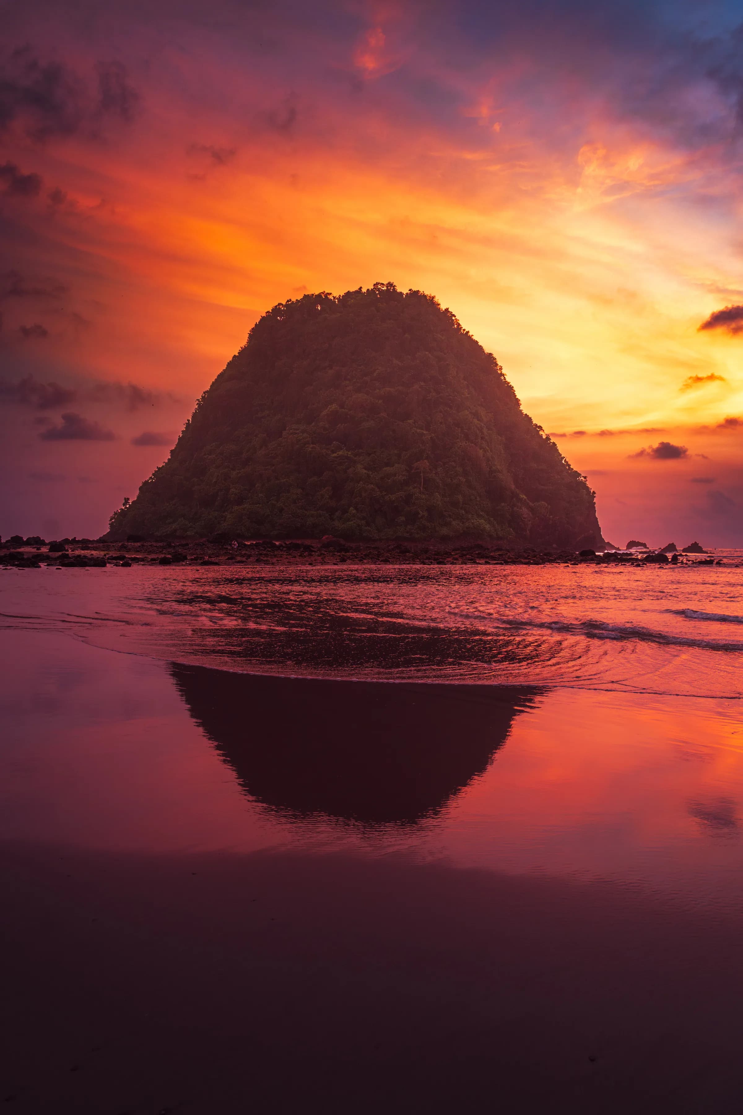 Pulau Merah's red island silhouetted in a mirror-still sunset